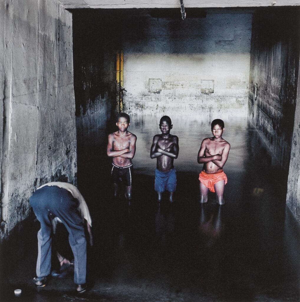 While Fernando Augusto Luta washed his clothes, Augusto Mokinda (13), Ze Jano (12) and Ze Ndala (10), posed for a photograph in water that has risen from underground in an old mineshaft at Pomfret Asbestos Mine. The water probably contained blue asbestos fibres. 25 December 2002.