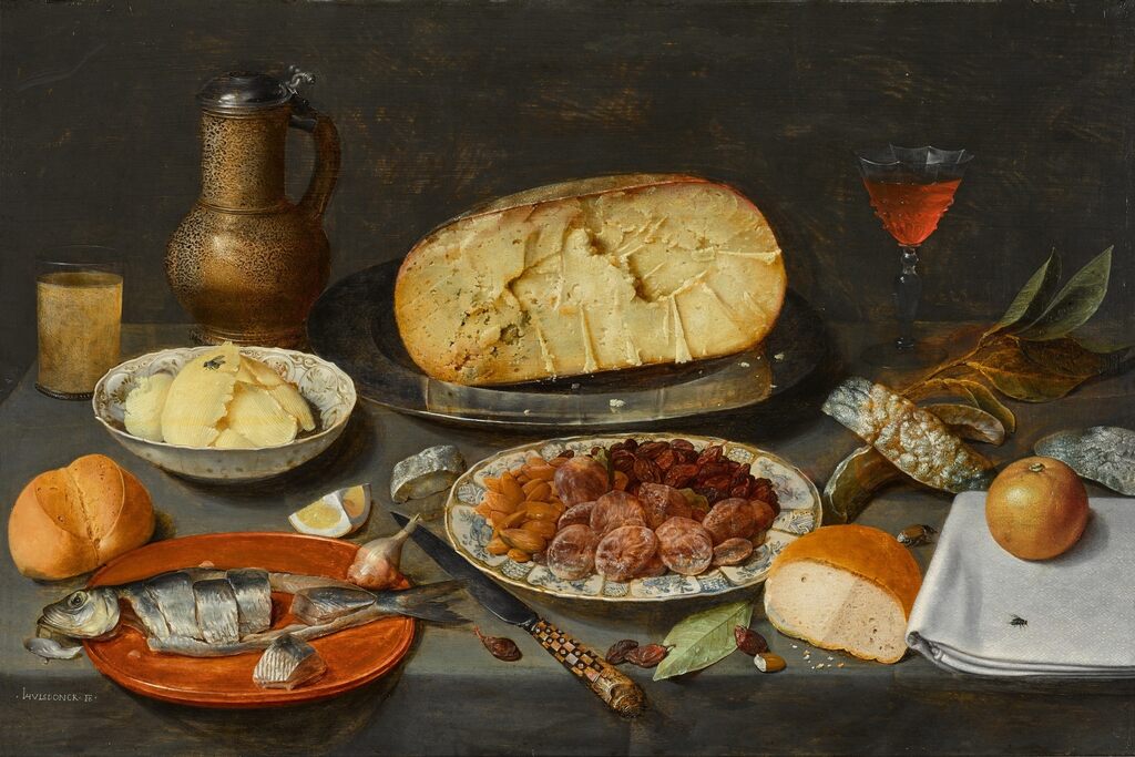 Still life with a herring, cheese, preserved fruits and nuts, bread, butter, and a wineglass and jug, all on a draped table