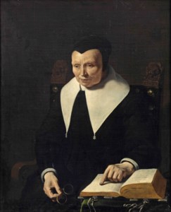 Portrait of an old lady, half-length, seated in a chair holding her glasses and pointing at a book on a table