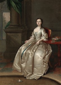 Portrait of a Lady, full-length, seated in a white satin dress, beside a table with a basket of flowers, a sprig of orange blossom in her right hand, in an interior