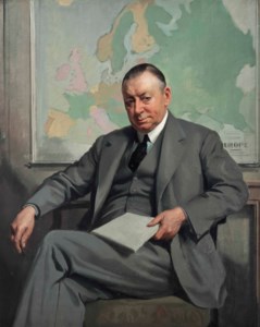 Portrait of Edward Verrall Lucas (1868-1938), seated three-quarter-length, in a grey suit and tie, with a map of Europe