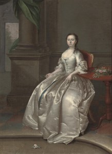 Portrait of a lady, seated, full-length, in a white dress, beside a table with a basket of flowers, a sprig of orange blossom in her right hand, in an interior
