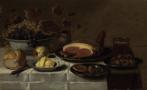 White and blue grapes in a 'kraak' porcelain bowl, a loaf of bread, a knife, butter on a porcelain plate, a biscuit and medlar on a silver plate, a mug of beer, a joint of ham on a third silver plate, a ceramic jug and apples, all on a draped table