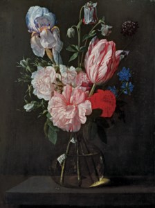 A tulip, roses, iris and other flowers in a glass vase on a ledge