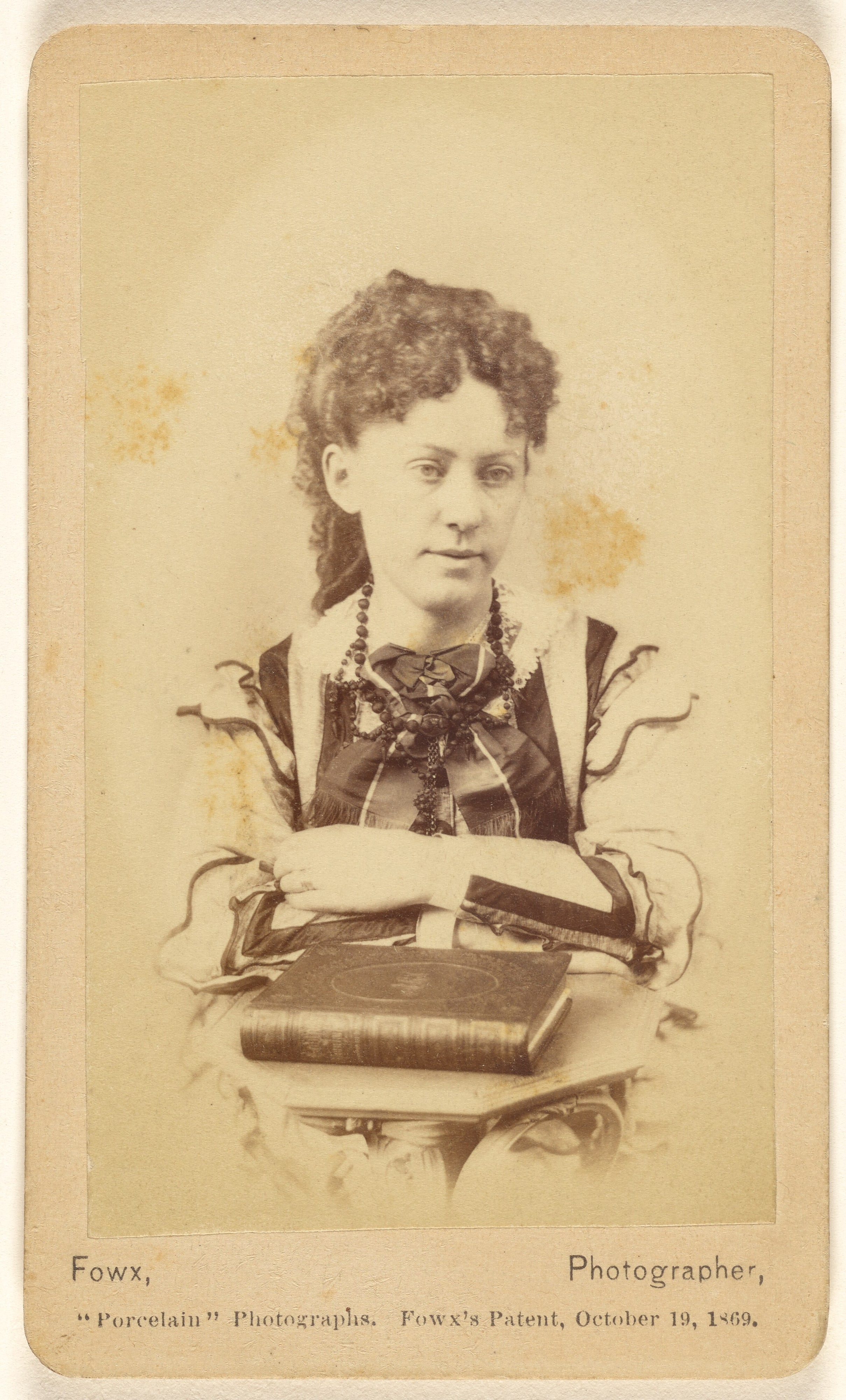 [Unidentified woman seated with arms crossed, books in foreground]