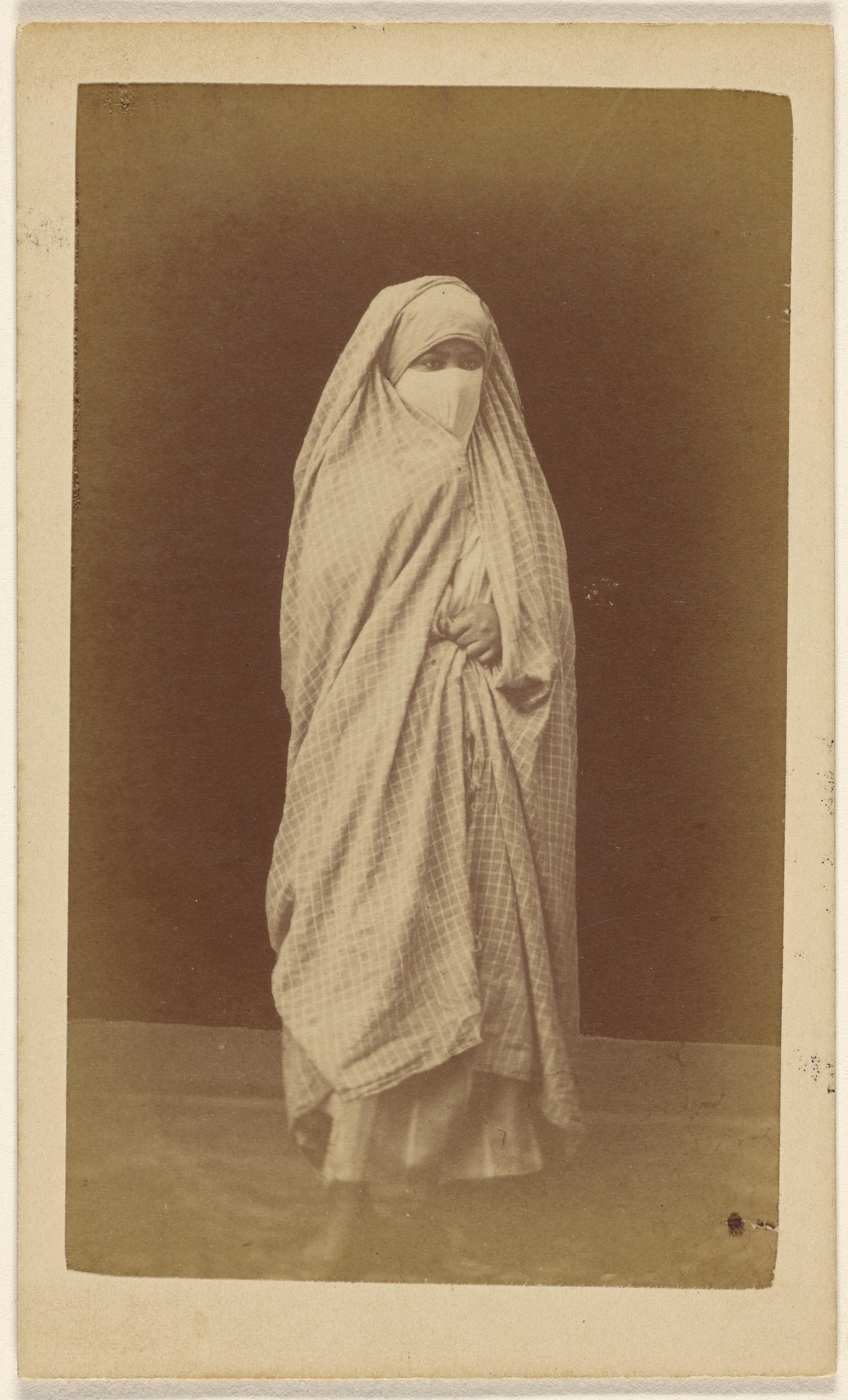 [Unidentified Algerian woman wearing a checkered full robe and veil]