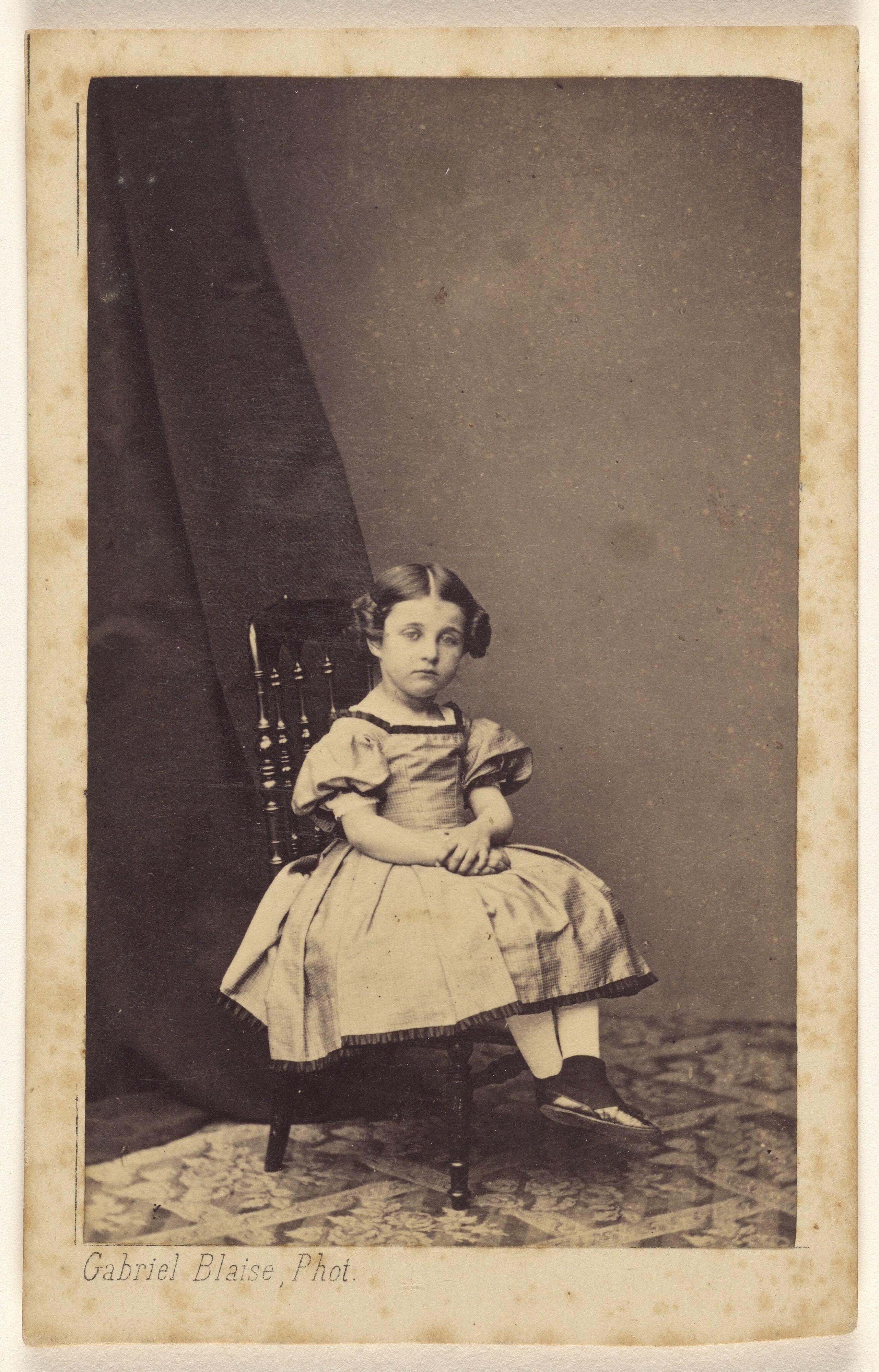 [Unidentified little girl with hair up on both sides, seated, with hands clasped]
