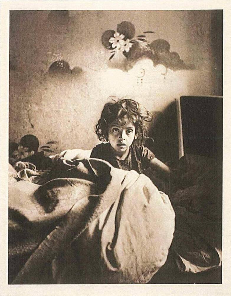 [Sara, sitting in bed in a basement dwelling, with stenciled flowers above her head, Warsaw]