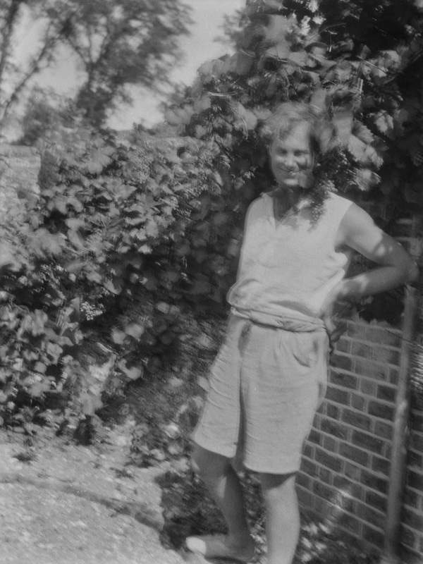 ‘Black and white negative of Julian Bell wearing shorts and standing in the walled garden at Charleston, Firle, Sussex