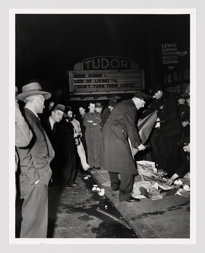 This man covered up with newspapers was killed in an auto accident. The driver of the car was arrested, but he put up such a terrific battle...cops had to put handcuffs on him.