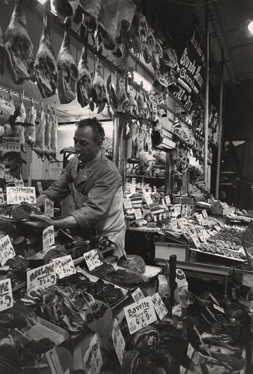 Affluences in Europe: in France, prosperity immediately translates itself into good food. The variety of cuts of meat sold in the market is staggering: everything from barbecued chickens to calf hearts, from the lushest whole hams to tripe is lovingly displayed in neat rows decorated with green leaves and herbs, a butcher-shop in Paris