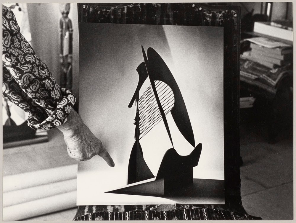 Main de Pablo Picasso montrant la photographie de la maquette de la sculpture "Tête" pour le Chicago Civic Center (Daley Center), à Notre-Dame-de-Vie, Mougins, en août 1966