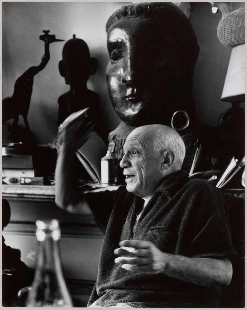 Portrait de Pablo Picasso de profil et faisant un geste de la main, à côté des sculptures "Tête de femme (Dora Maar)" et "Grue" posées sur un buffet, à La Californie, Cannes, en 1956