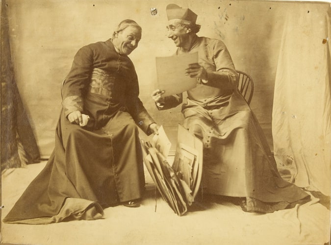 Deux hommes assis vêtus de costumes sacerdotaux, consultant un portefeuille d'images