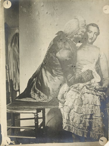 Homme costumé en courtisan à la cour de Louis XV, assis, de dos, embrassant un mannequin féminin en bois et chiffon, vêtu d'une jupe de dentelle